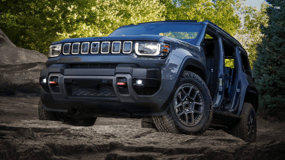 2026 Jeep Recon in Margate FL in dark gray with squared-off seven-slot grille, LED headlights, heavy-duty off-road tires, and flared fenders crawling over rocky terrain