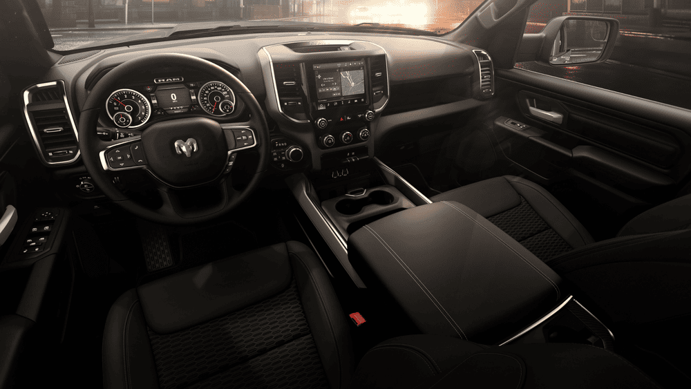 2026 Ram 1500 Rebel interior in Margate FL with RAM-branded steering wheel, analog dual-gauge cluster, touchscreen infotainment with navigation, and all-black dashboard and center console