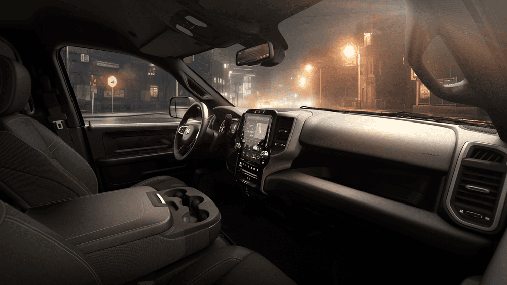 2026 Ram Heavy Duty interior in Margate FL showing RAM-branded steering wheel, large vertical center touchscreen, dark gray dashboard, and black seats photographed at night with city lights visible