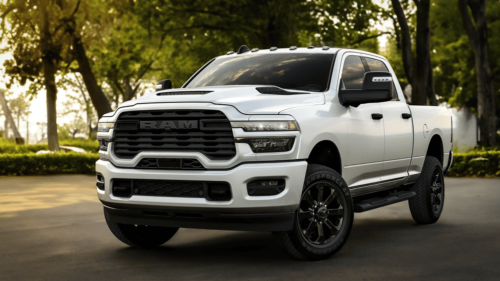 2026 Ram Heavy Duty in Margate FL in white with oversized black RAM grille, LED headlights, hood scoop, black alloy wheels, and crew cab body parked on a shaded street