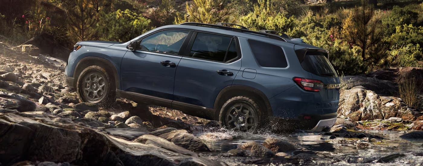 Rear of a grey 2026 Honda Pilot driving off-road up a hill.