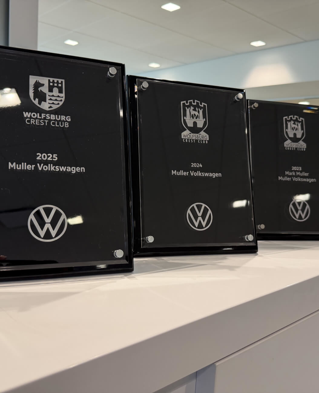 Three Muller Volkswagen Wolfsburg Crest Club awards for 2023, 2024 and 2025 displayed on a counter.