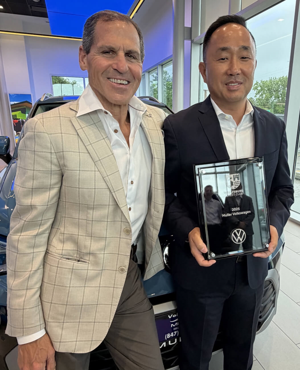 Two Muller Volkswagen representatives pose with the 2025 Wolfsburg Crest Club Award.