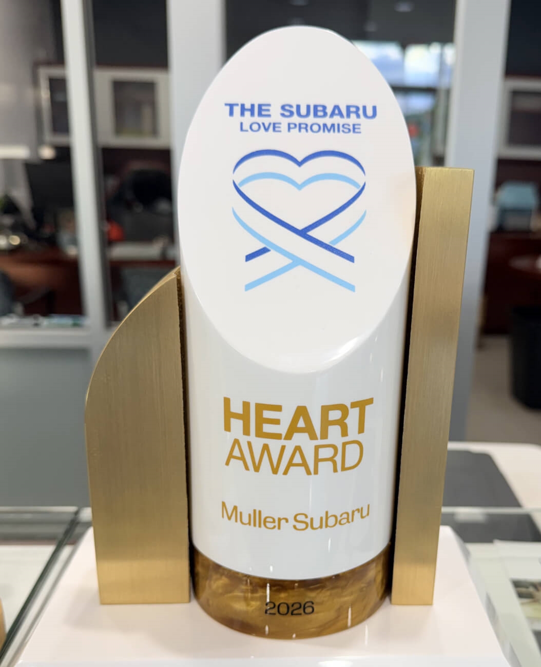 Muller Subaru team poses around the 2026 Subaru Love Promise Heart Award inside the dealership.