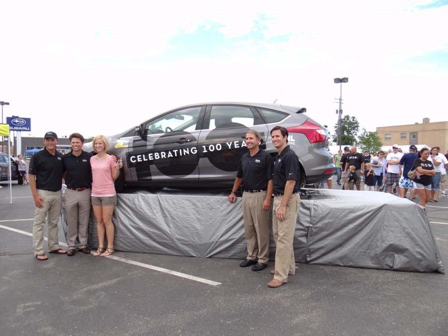 People standing in front of a car labeled Celebrating 100 Years