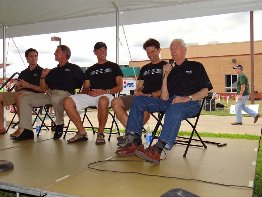 Several Dahl family members seated on a stage while an older man addresses the crowd