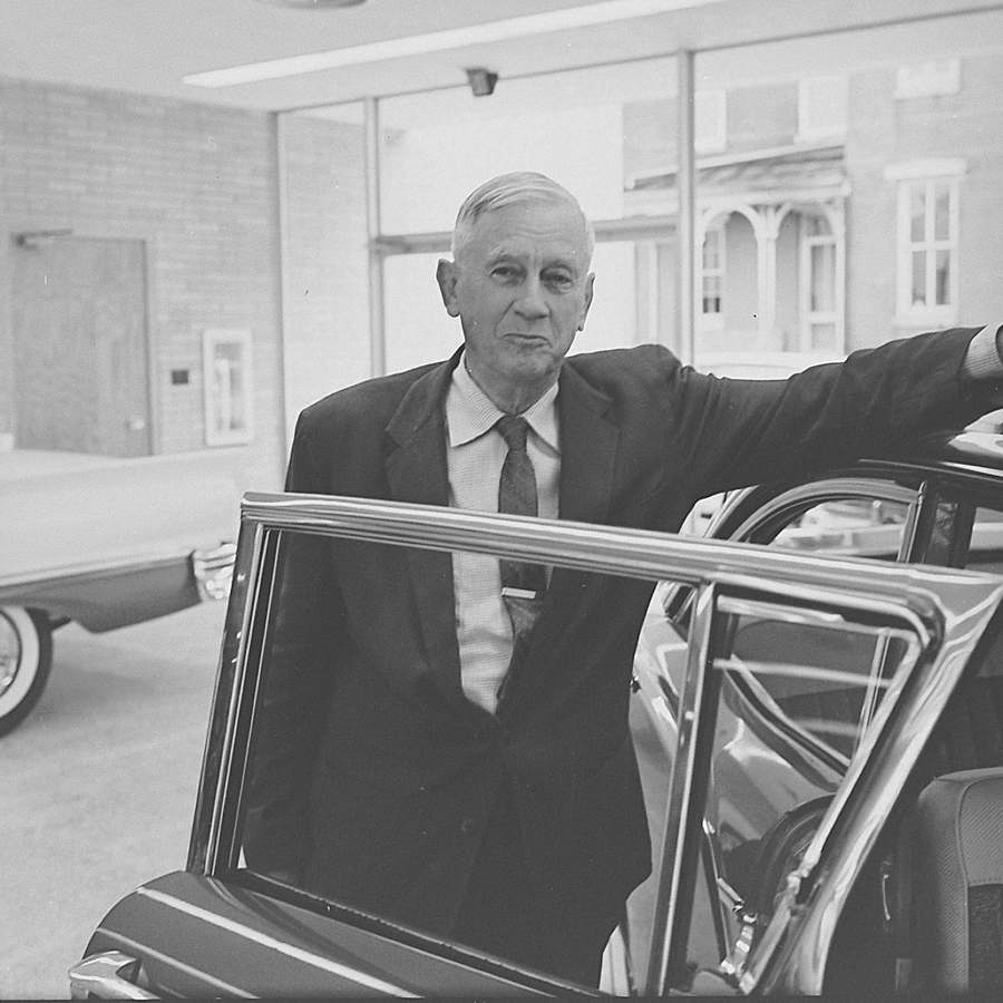 Harry J. Dahl standing beside an open car door inside a dealership showroom