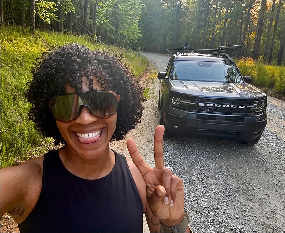 First-time buyer standing in front of her new Ford Bronco Sport on a forest road