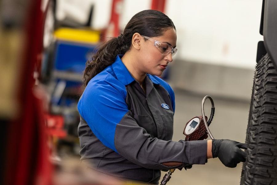 Ford technician performing an oil change underneath a vehicle on a lift in a dealership service center.