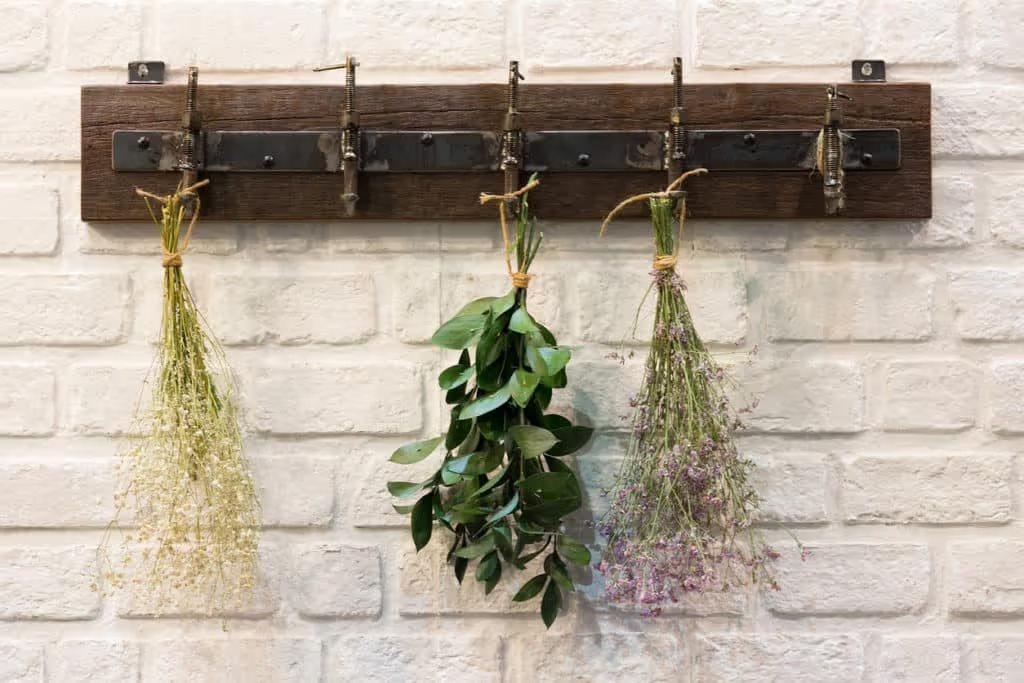 Wooden vintage style Hanger / Hooks on white brick wall decorated with dried bouquets in a country style home.