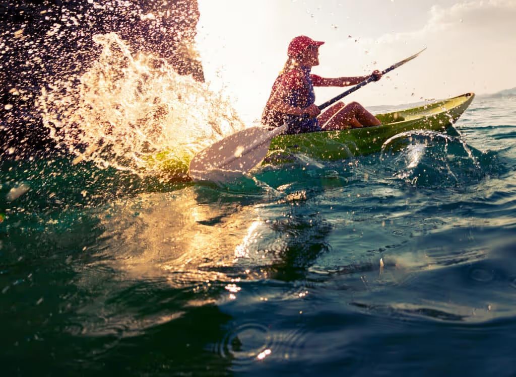 kayaker splashing in choppy water with sun glowing in the spray