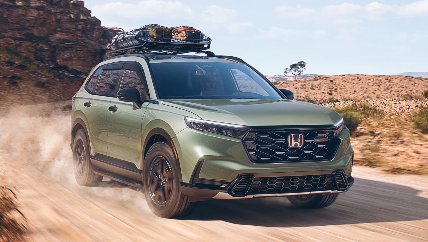 Green Honda CR-V TrailSport driving on a desert road with cargo secured to the roof rack.
