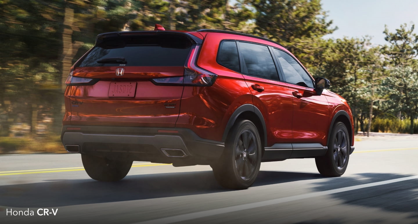 Red Honda CR-V driving on a tree-lined road.