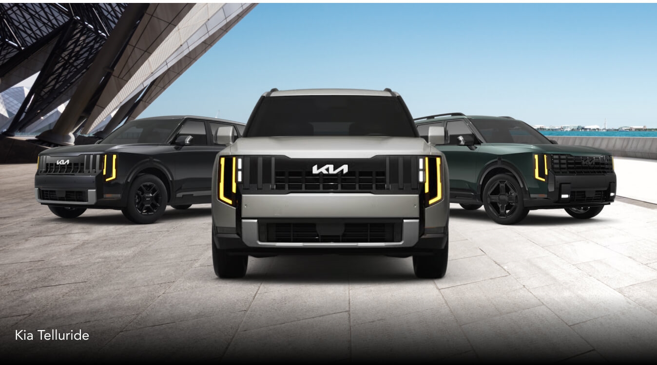 Three KIA Tellurides, in LX, ES and X-Line EX trims, parked side-by-side in a modern urban building's parking lot.