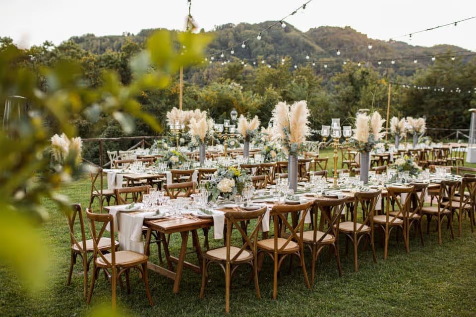 A wedding table set up in the woods. Boho vibe. Greenery, glass, pampas grass, white linens.