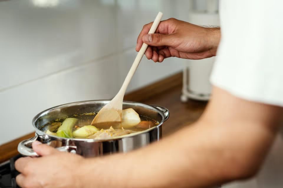 Man stirs soup cooking on the stove.