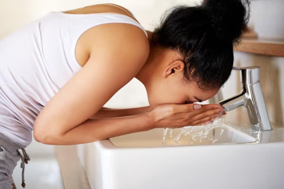 Young woman washing her face at a bathroom sink