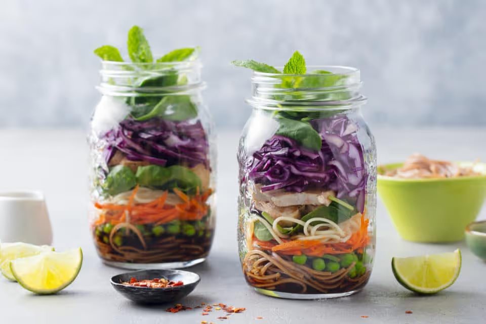 Healthy asian salad with noodles, vegetables, chicken and tofu in glass jars. Grey background