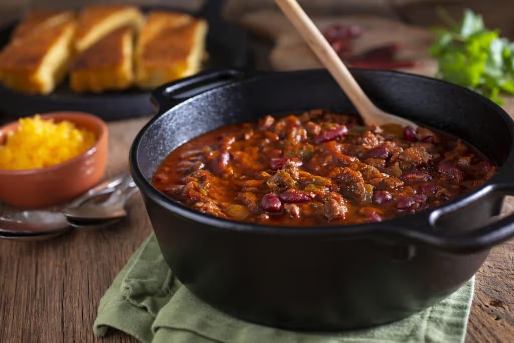 a cast iron bowl of chili with bread blurred in the background