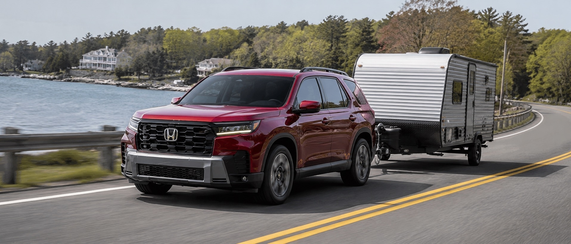 2026 Honda Pilot towing a small camper trailer on a waterfront road