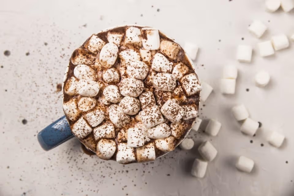 Hot chocolate full of marshmallows in a blue mug. Cocoa powder is sprinkled over the top of the marshmallows. 