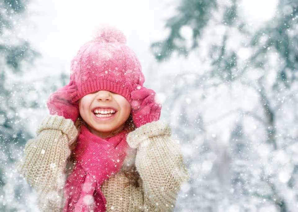Happy child wearing a tan coat, pink hat, and pink scarf playing on a winter walk in nature