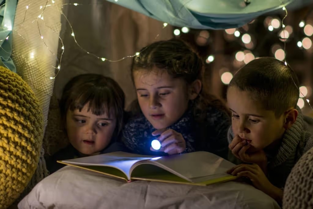 children reading book in pillow fort