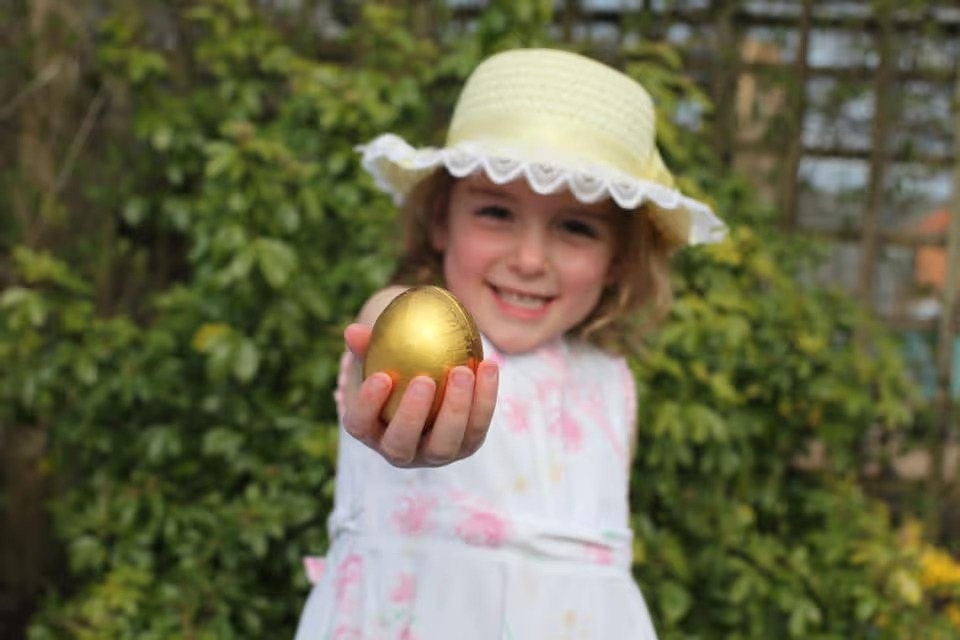 Girl in easter bonnet and dress after an egg hunt. She is holding a golden easter egg.