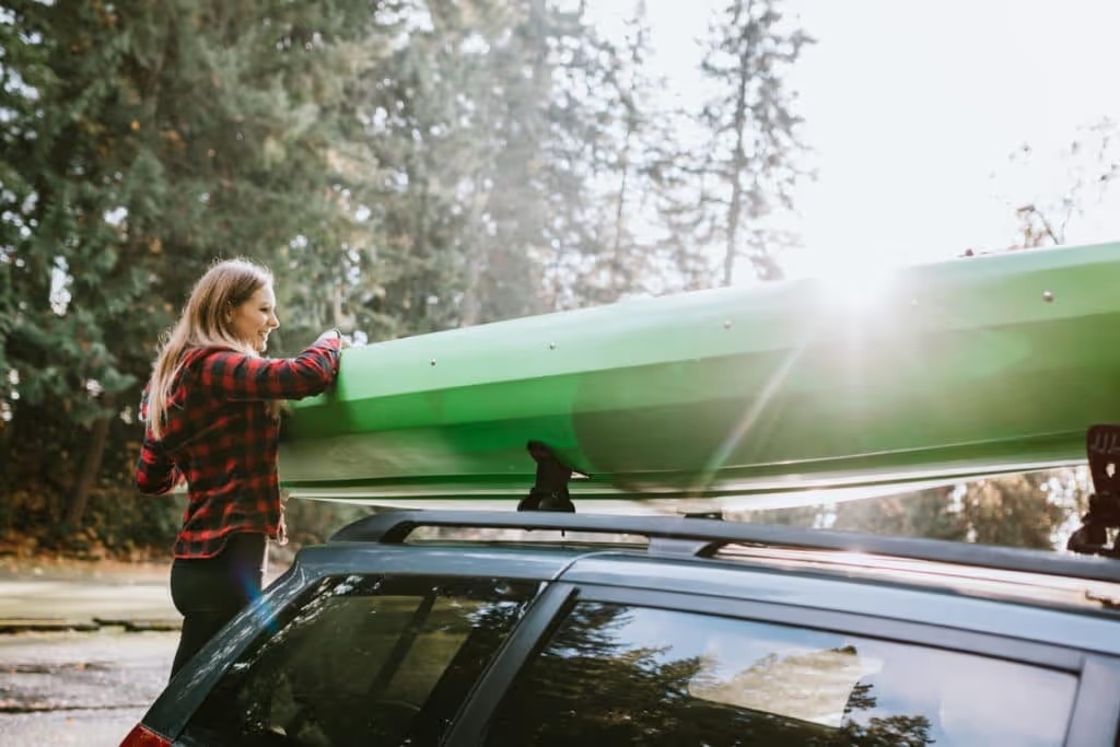 woman loads kayak onto roof of vehicle