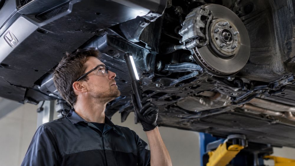 Technician visually inspecting a Honda underbody for corrosion
