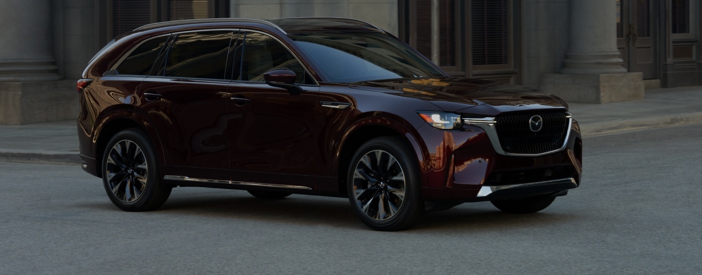 Red 2026 Mazda CX-90 driving down a city street.