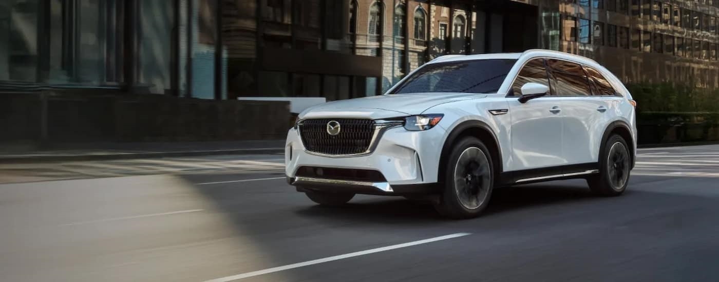 White 2026 Mazda CX-90 driving down a city street.