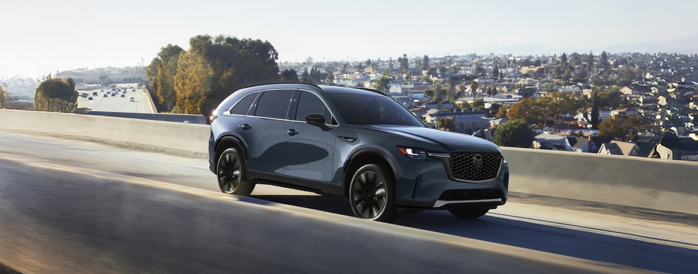 Grey 2026 Mazda CX-90 driving down an open road.
