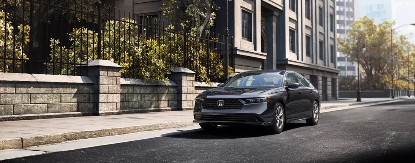 Black 2023 Honda Accord EX driving by a fence.