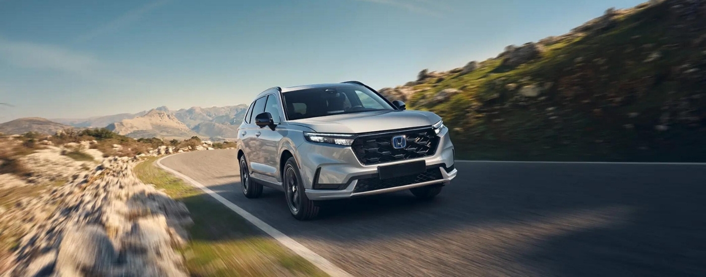 A white 2025 Honda CR-V Hybrid driving on a paved mountain road.