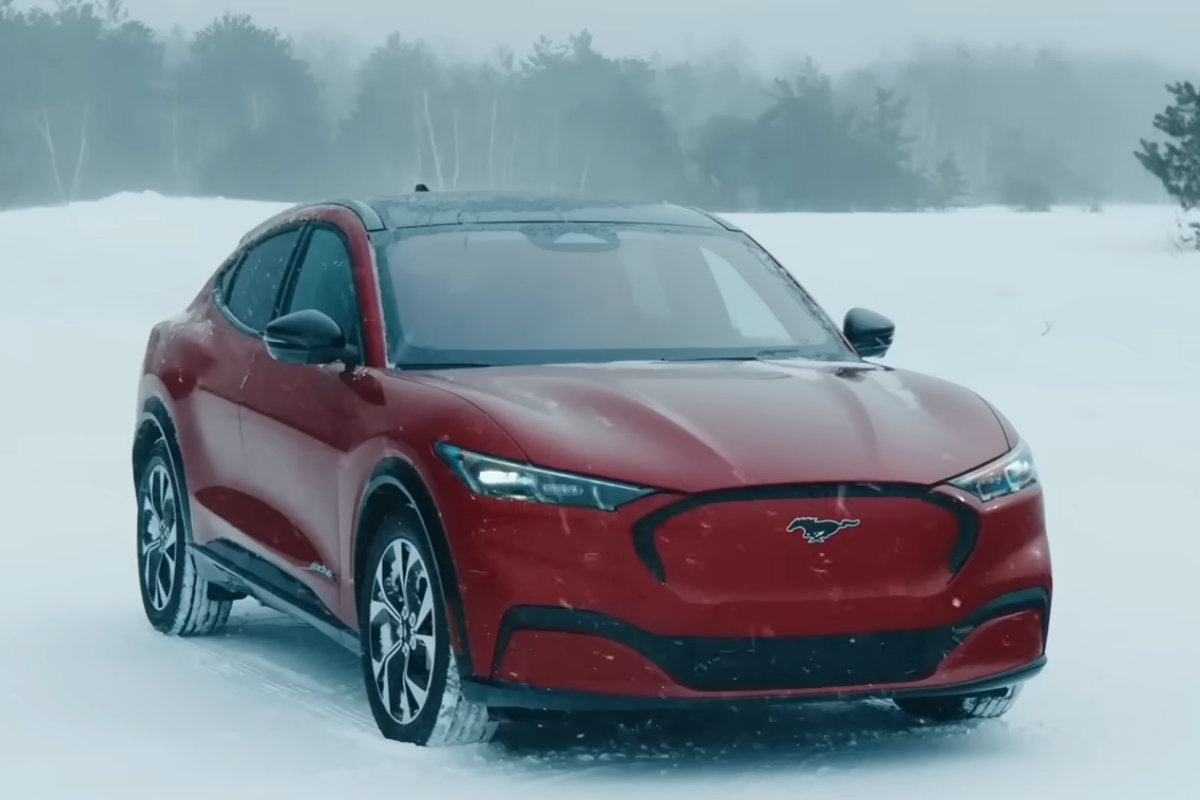 Red Ford Mustang Mach-E driving through snowy winter conditions.