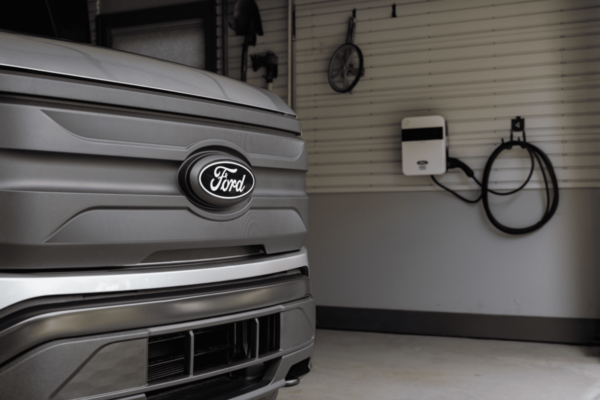 Ford electric vehicle parked in a garage with a wall-mounted home EV charger in the background.