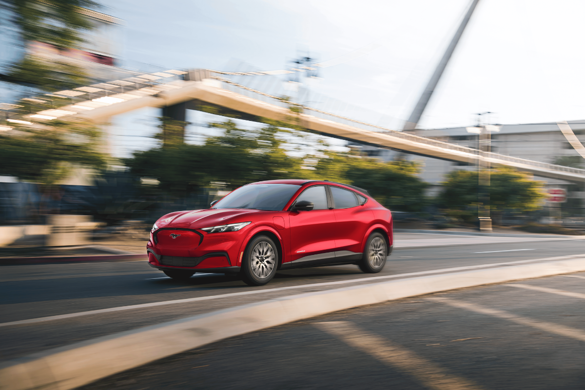 Red Ford Mustang Mach-E electric SUV driving through a city street.