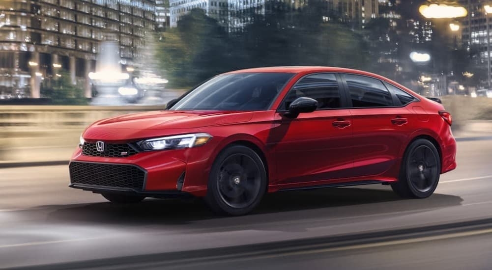 A red 2026 Honda Civic Si driving in a city.
