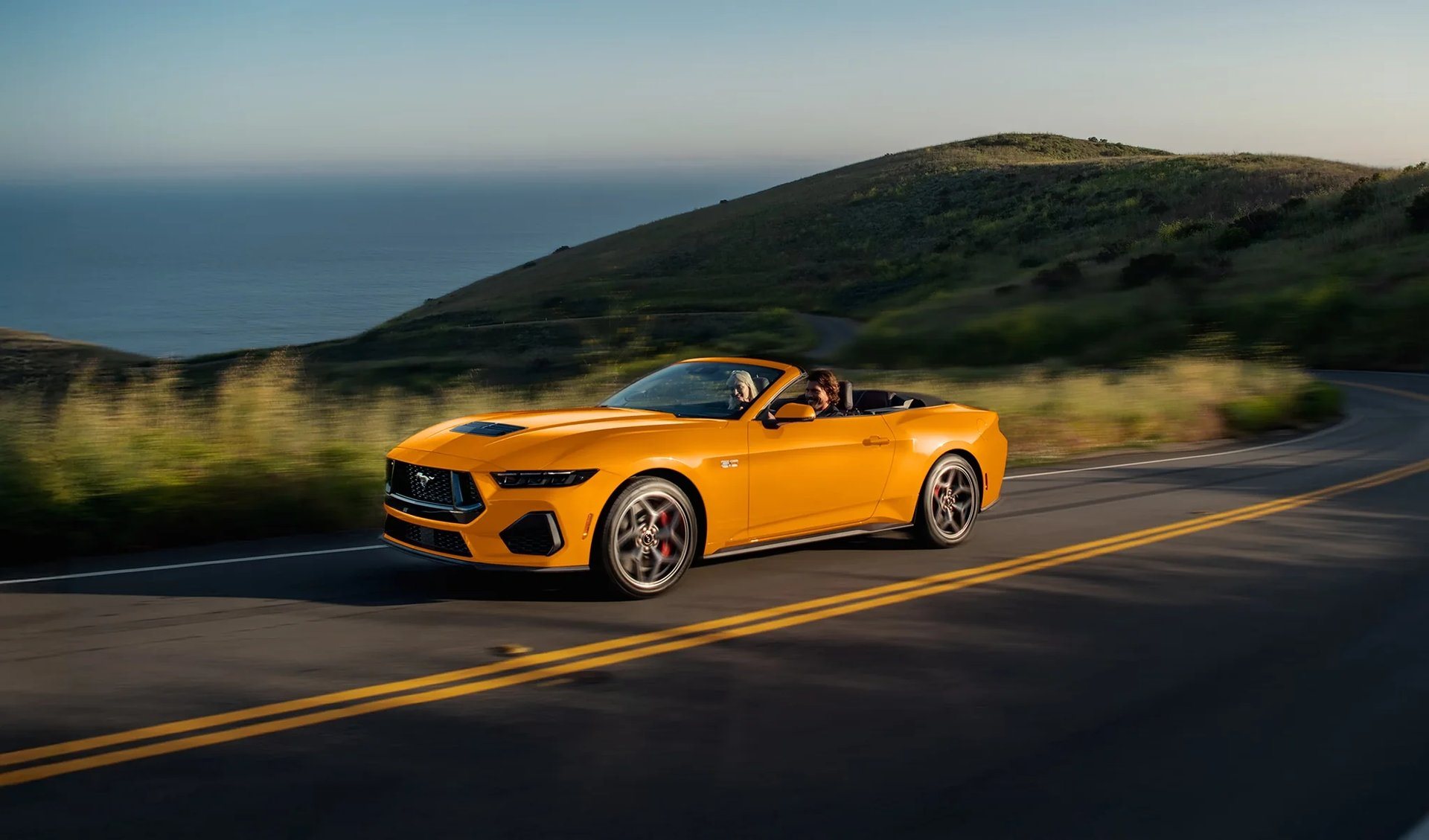 Two people driving a current Ford Mustang GT convertible on a coastal road