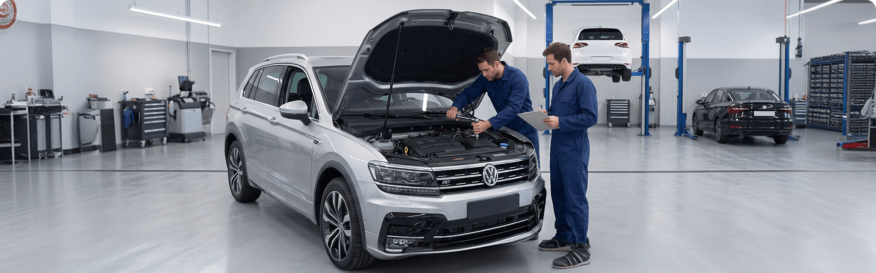 Two Volkswagen technicians inspecting the engine bay of a silver Volkswagen Tiguan, one reviewing a checklist on a clipboard