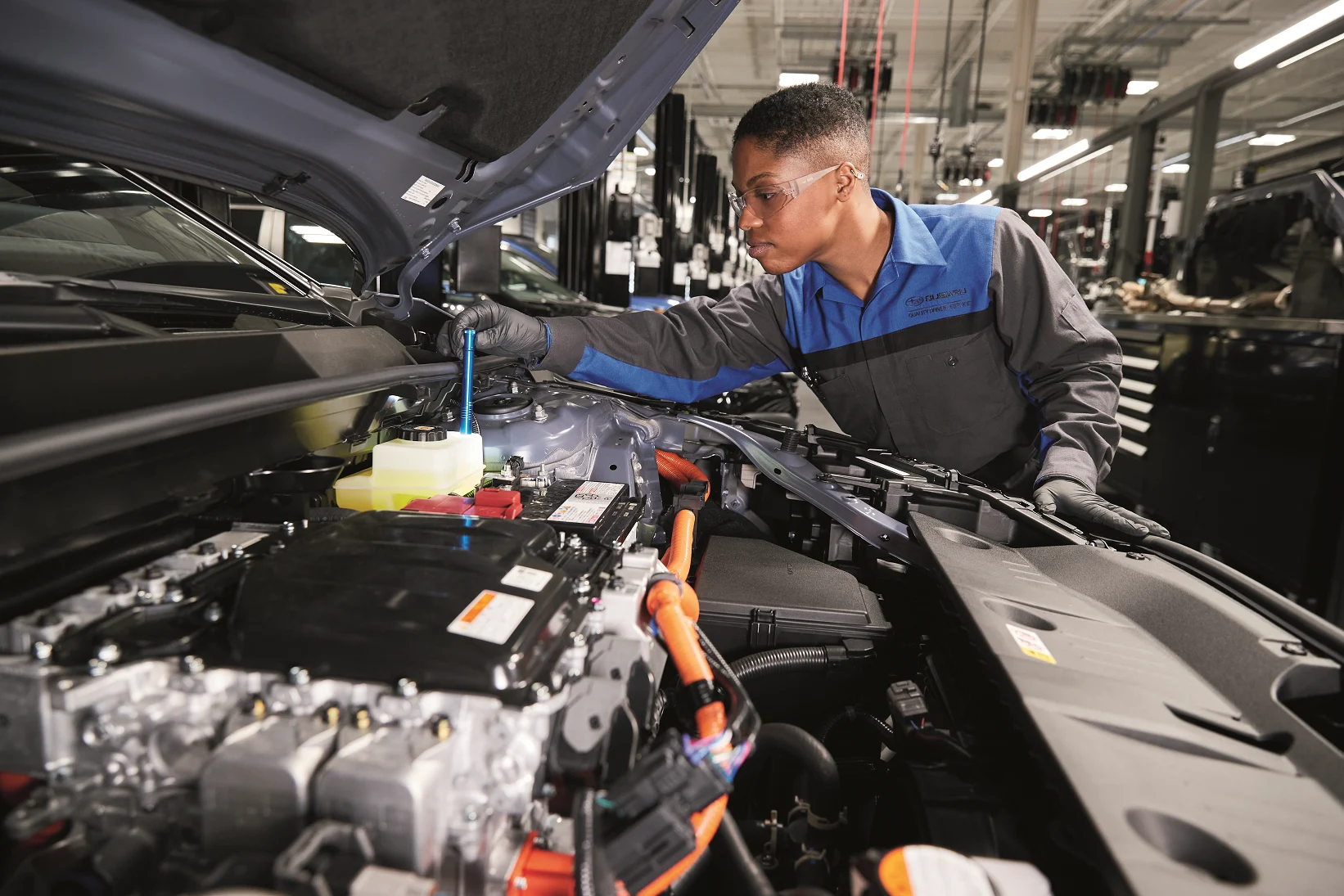 A Findlay Subaru Prescott technician in a Subaru service uniform working under the hood of a Subaru in the service shop.