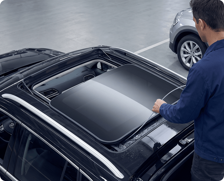 Technician inspecting the seal and track of an open sunroof on a black Volkswagen