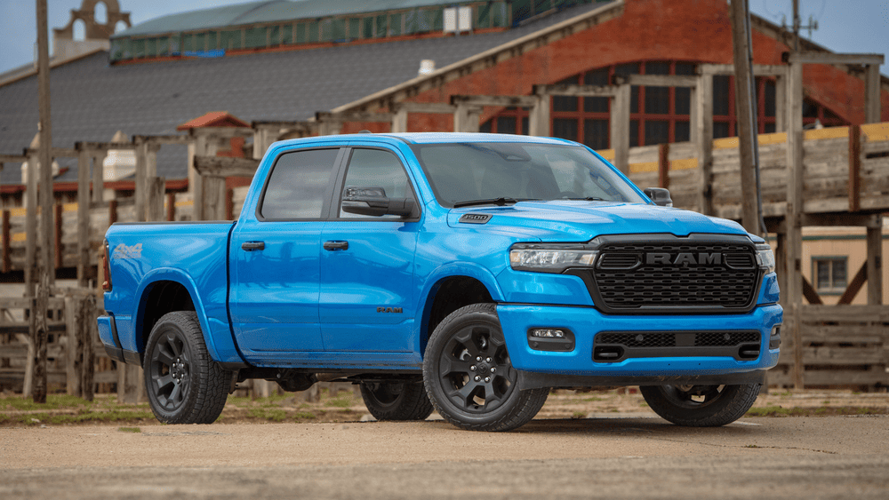 2026 Ram 1500 in Margate FL in blue with black RAM grille and blacked-out wheels by a ranch fence