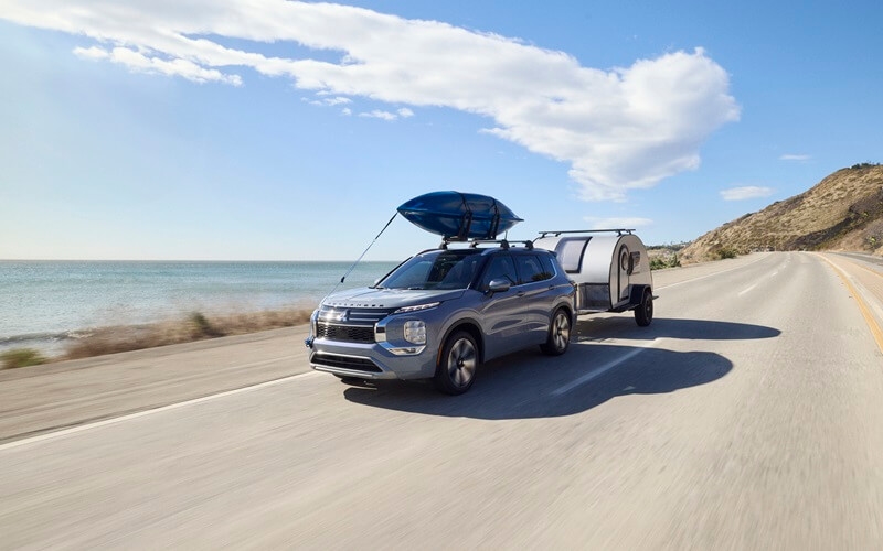 A 2025 Mitsubishi Outlander tows a trailer along a ocean road