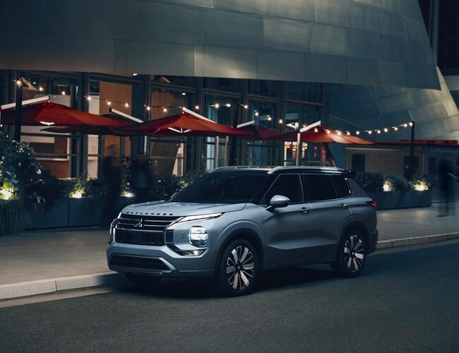 A 2025 Mitsubishi Outlander is parked outside of a restaurant at night