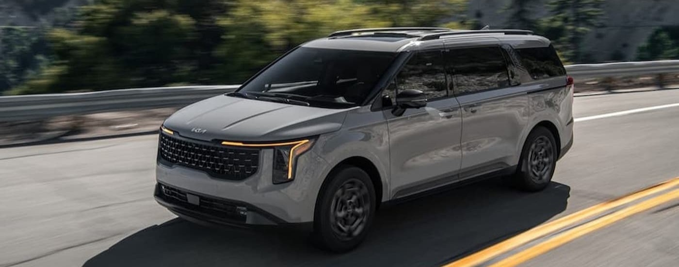 A gray 2025 Kia Carnival driving on a highway.