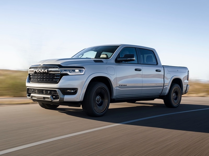 A gray 2026 Ram drives down a road with bright sunlight.