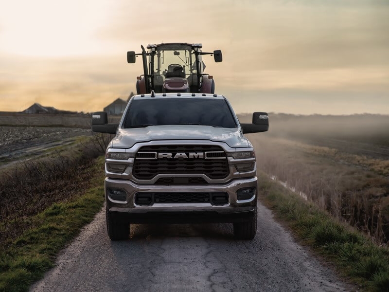 A head-on shot of a gray 2026 Ram 2500 hauling farming equipment.