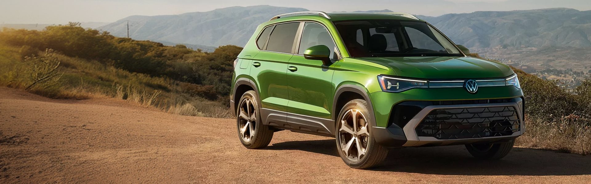 Green 2027 Volkswagen Taos parked on a dirt overlook with mountains behind it